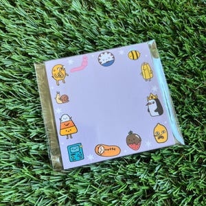 May include: A purple card with a variety of cartoon characters, including a snail, a penguin, a candy corn, a lemon, a strawberry, a worm, a bee, a game console, and a sleeping figure. The card has a white border and a white background with white stars.