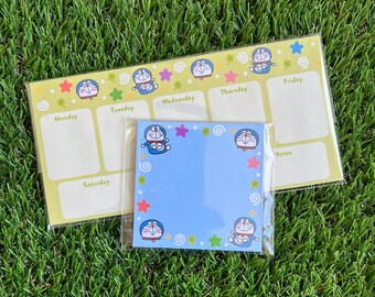 May include: A weekly planner and a blue sticky note pad featuring the cartoon character Doraemon. The planner is light yellow with days of the week labels. The sticky note pad is blue with Doraemon illustrations and star accents.