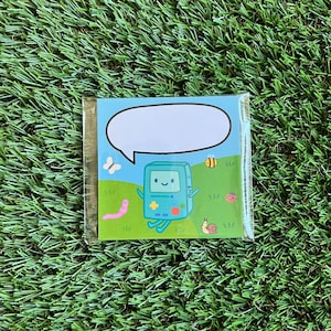 May include: A green and blue cartoon character with a speech bubble above its head. The character is standing in a green field with a pink worm, a bee, and a snail. The background is blue.