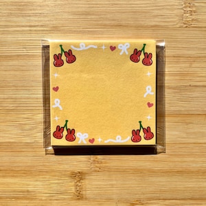 May include: A pack of yellow sticky notes with a border of red cherries and white bows. The notes are packaged in a clear plastic sleeve.