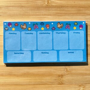 May include: A blue weekly planner with a colorful border of pixelated animal and plant designs. The planner has sections for Monday through Sunday and a notes section.