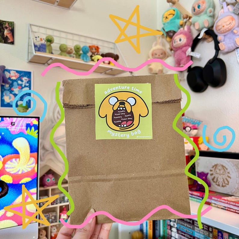 Op de afbeelding: Een bruine papieren zak met een sticker waarop een cartoonhond te zien is met de tekst "adventure time mystery bag".