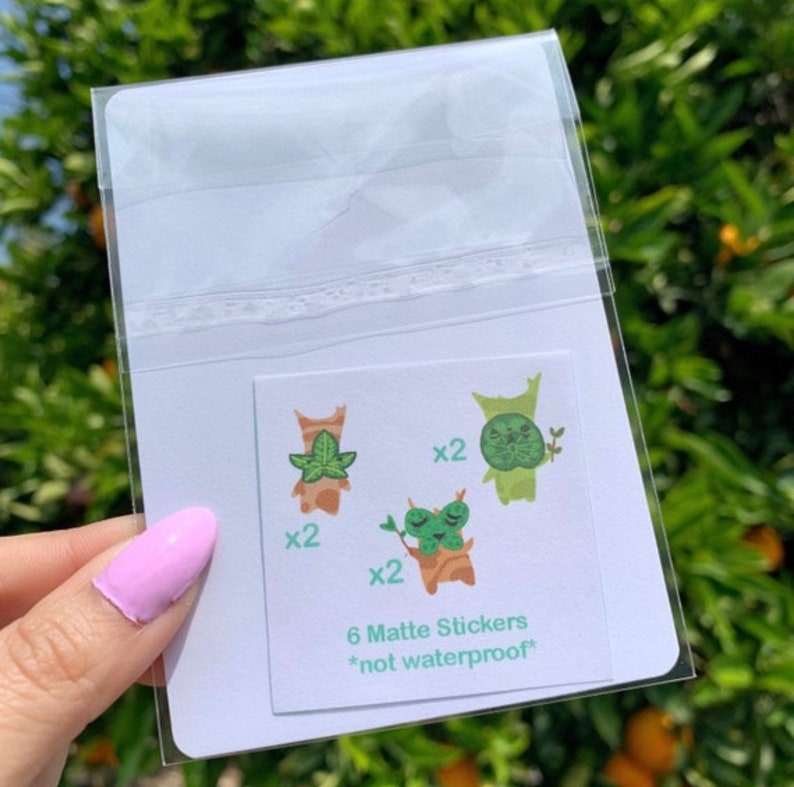 May include: A clear plastic bag containing six matte stickers featuring cartoon illustrations of green and brown creatures with leaves. The stickers are not waterproof and are labeled "6 Matte Stickers *not waterproof*"