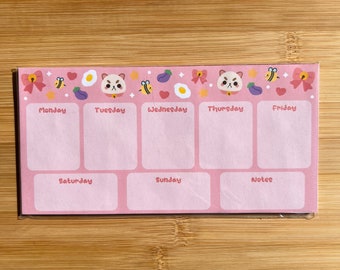 May include: Pink weekly planner featuring a cute cartoon cat design. The planner has spaces for each day of the week, including Monday, Tuesday, Wednesday, Thursday, Friday, Saturday, Sunday, and a notes section.