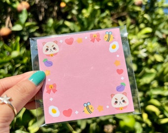 May include: Pink sticky note pad with a cute cartoon animal border. The border features a cat, a bee, a heart, a star, a bow, and an egg.