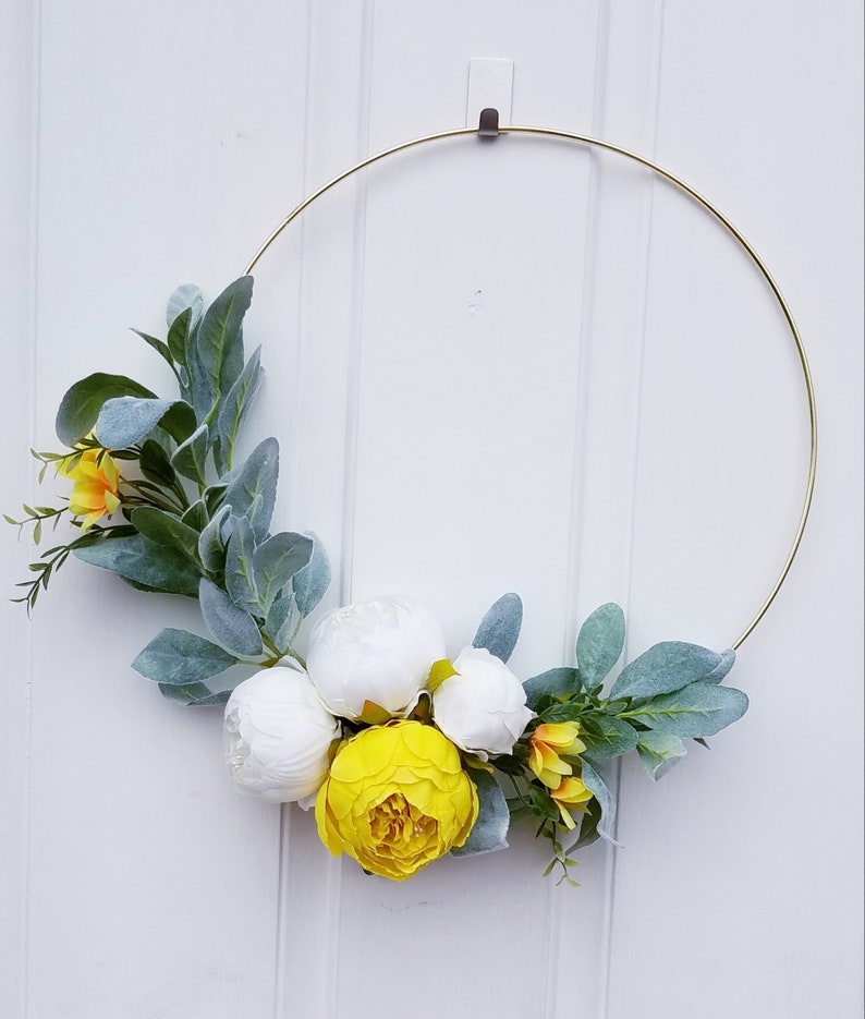 May include: A gold metal wreath with white and yellow artificial flowers. The wreath is decorated with green leaves.