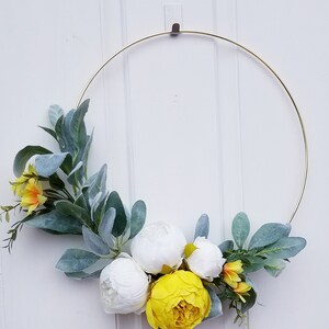 May include: A gold metal wreath with white and yellow artificial flowers and green leaves.