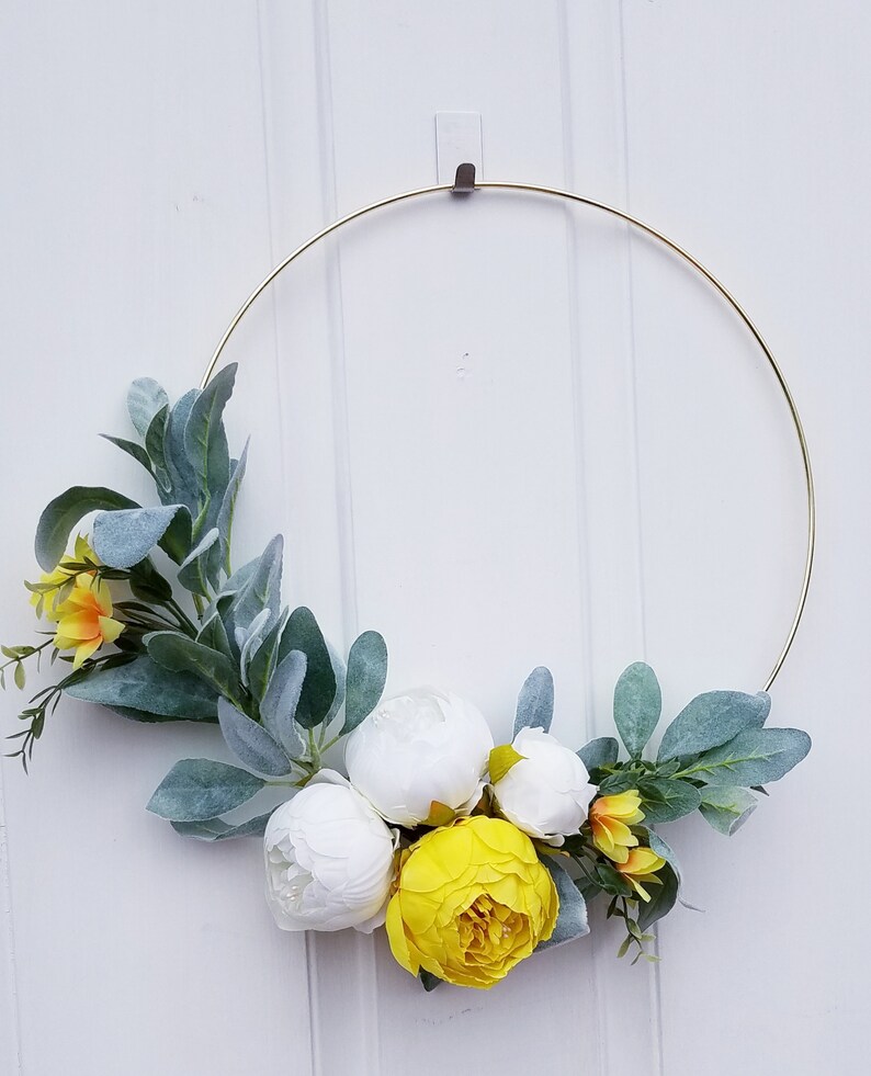 May include: A gold metal wreath with white and yellow artificial flowers and green leaves.