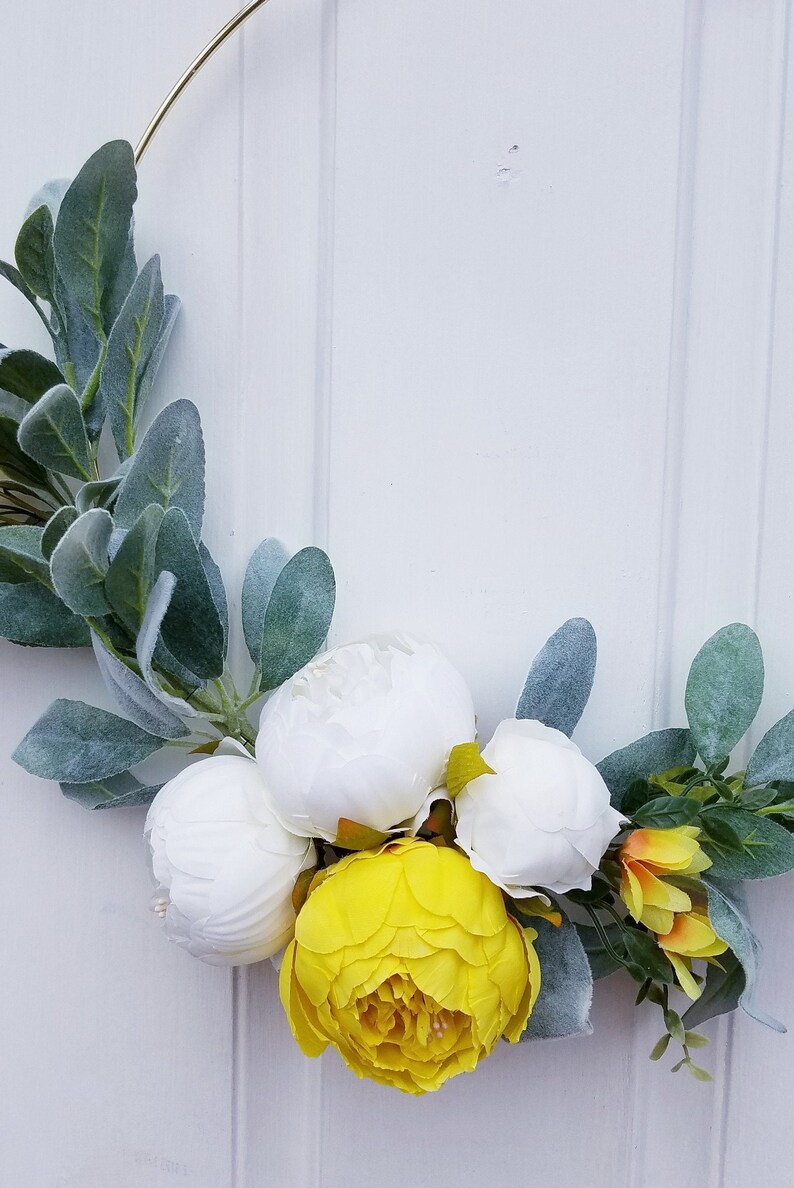 May include: A wreath made with white and yellow flowers and green leaves. The wreath is on a white background.