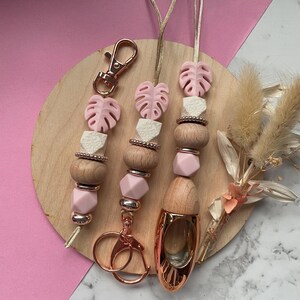 Pode incluir: Lanyards de contas rosa e de madeira, com fechos e chaveiros dourados. Os lanyards apresentam contas rosa em forma de folha, contas geométricas brancas e contas de madeira. Um difusor de óleos essenciais dourado também está incluído.
