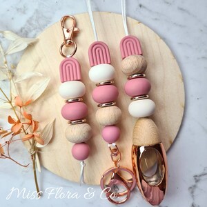 Pode incluir: Um chaveiro de contas rosa e branco com um fecho de ouro rosa e uma garrafa de difusor de ouro rosa. As contas são de madeira e silicone. O chaveiro está preso a um anel de chave de ouro rosa.