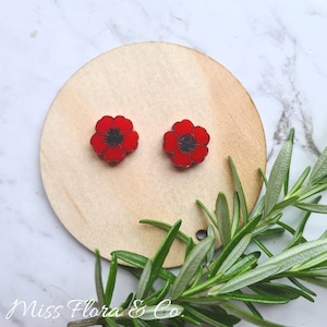 May include: A pair of red poppy flower stud earrings. The earrings are made of resin and have a black centre.
