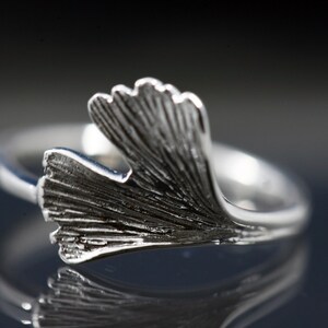 K&ouml;nnte beinhalten: Ein silberner Ring mit einem detaillierten Ginkgoblatt-Design. Das Blatt ist gebogen und scheint aus Metall zu sein.
