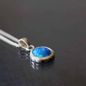 May include: A silver chain necklace with a blue opal pendant. The pendant is set in a silver bezel and has a round shape.