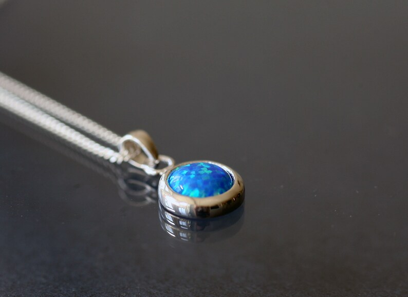 May include: A silver chain necklace with a blue opal pendant. The pendant is set in a silver bezel and has a round shape.