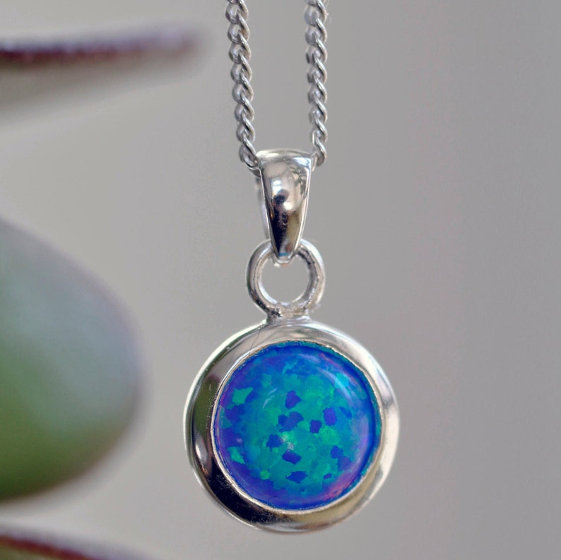 May include: A silver chain necklace with a round pendant featuring a blue opal gemstone.