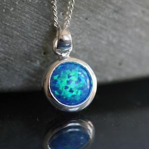 May include: A silver necklace with a round blue opal pendant. The opal has a green and blue iridescent sheen.