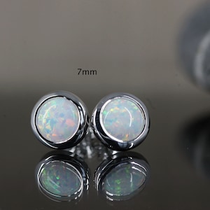 Könnte beinhalten: Ein Paar silberne Ohrstecker mit weißen Opal-Steinen. Die Steine haben einen Durchmesser von 7 mm.