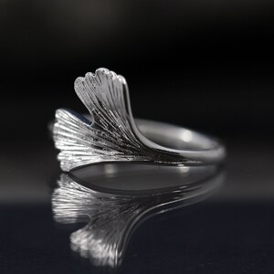 K&ouml;nnte beinhalten: Ein silberner Ring mit einem Ginkgoblatt-Design. Der Ring ist zart und hat eine polierte Oberfl&auml;che.