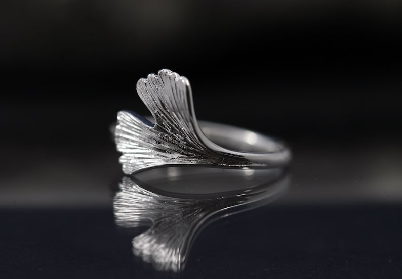 K&ouml;nnte beinhalten: Ein silberner Ring mit einem Ginkgoblatt-Design. Der Ring ist zart und hat eine polierte Oberfl&auml;che.