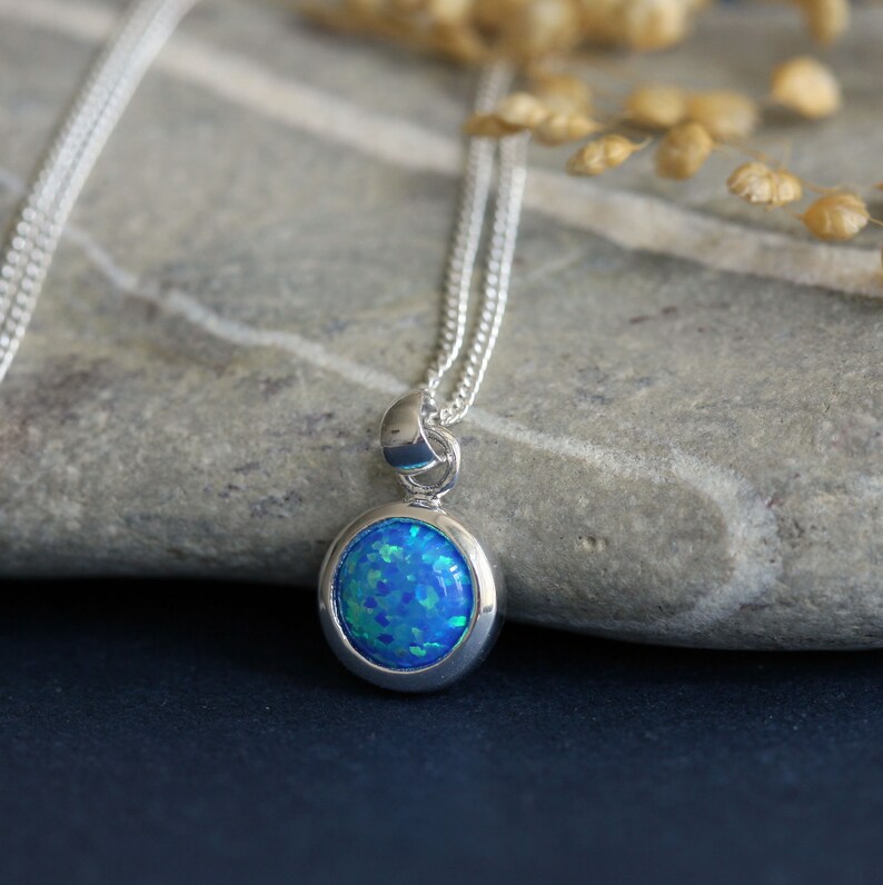 May include: A silver chain necklace with a blue opal pendant. The pendant is oval shaped and set in a silver bezel.