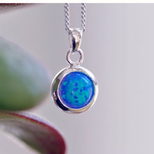 May include: A silver chain necklace with a round pendant featuring a blue opal gemstone.