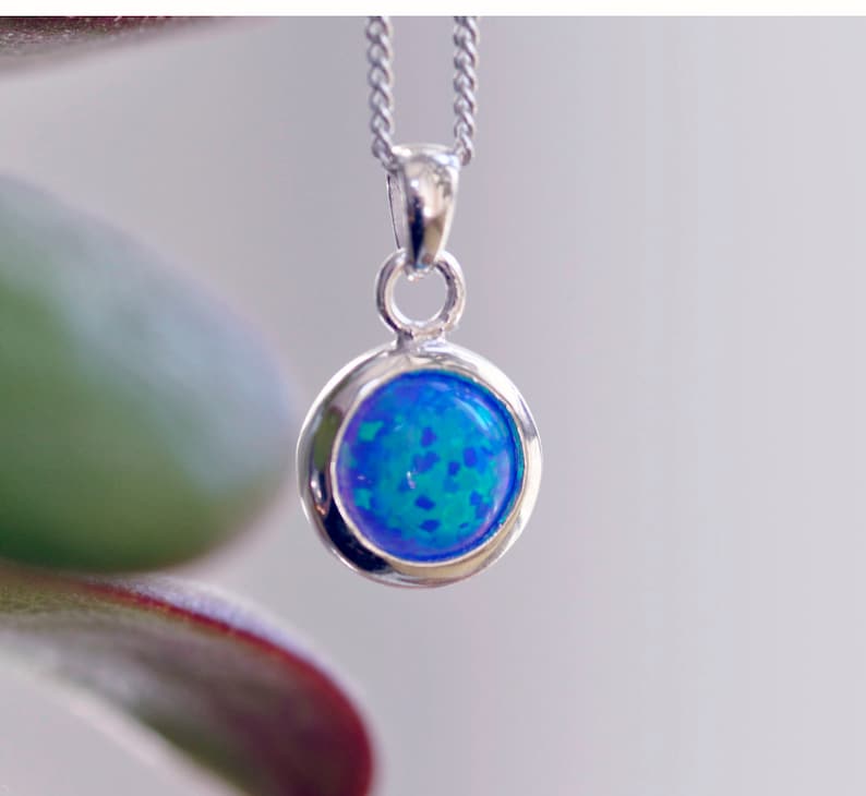 May include: A silver chain necklace with a round pendant featuring a blue opal gemstone.