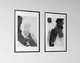 May include: Two black and white abstract art prints in black frames hanging on a white wall above a white couch with black throw pillows.
