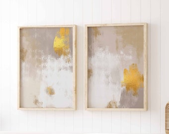 May include: Two abstract paintings in wooden frames with a white background and gold accents hang above a white bed with white bedding and a magazine on top.