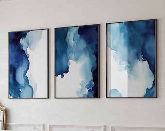 May include: Three abstract watercolour paintings in shades of blue, framed in black, hanging on a white wall above a white sofa.