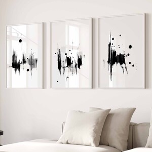May include: Three black and white abstract art prints with a white background and black brushstrokes. The prints are framed in white and are hung on a white wall.