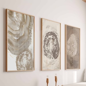 以下が含まれることがあります： ベージュ、ブラウン、ゴールドのニュートラルな色合いの木目デザインの3つの額入り抽象芸術プリント。アートワークは、クッション付きの木製プラットフォームの上にある白い壁に展示されています。部屋はミニマリストでモダンな美学を持っています。