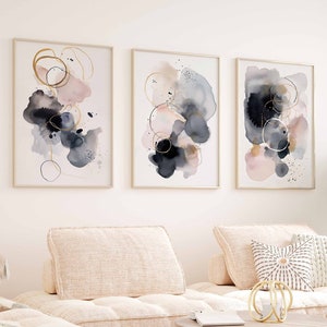 May include: Three abstract watercolour paintings in gold frames. The paintings feature pink, blue and black watercolour washes with gold circles and lines.