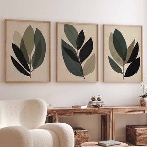 Puede incluir: Tres impresiones enmarcadas de diseños abstractos de hojas verdes sobre un fondo beige. Las impresiones están colgadas en una pared blanca sobre una mesa de madera y un sillón blanco.