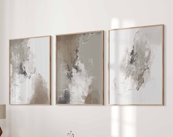 May include: Three abstract paintings in a minimalist bedroom setting. The paintings are framed in natural wood and feature muted tones of brown, gray, and white. The paintings are hung on a white wall above a bed with a beige blanket and a wooden side table.