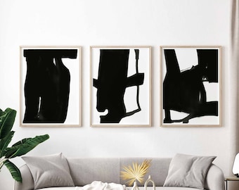 Könnte beinhalten: Drei Schwarz-Weiß-Abstrakte Kunstdrucke in Holzrahmen, die an einer weißen Wand über einem grauen Sofa mit einer weißen Wolldecke und einem Couchtisch mit einer Vase und einer Pflanze hängen.