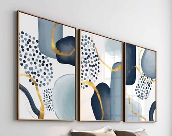 May include: Three abstract art prints with gold accents and blue and white geometric shapes. The prints are framed in a thin, gold frame and are hanging on a white wall above a bed.