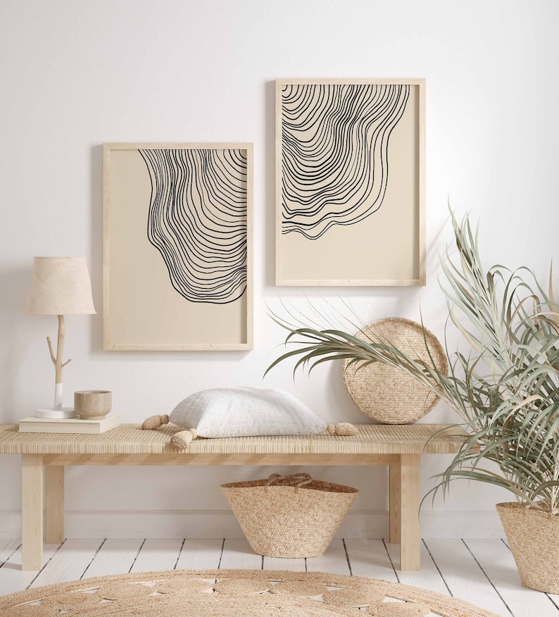 May include: Two framed black and white line art prints with a beige background. The prints are hanging on a white wall above a wooden bench with a white pillow. A potted plant with green leaves is on the right side of the bench.