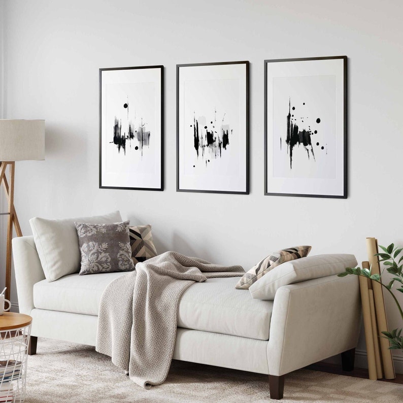 May include: Three black and white abstract art prints in black frames are hung on a white wall above a white couch with a gray throw blanket.