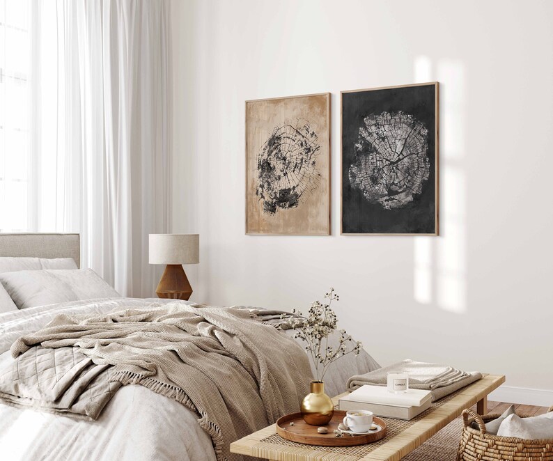 May include: Two framed black and white prints of tree rings on a white wall above a bed with a beige throw blanket and a wooden side table with a lamp.