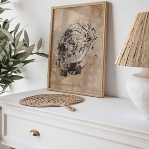 May include: A framed print of a black and white tree ring design on a beige background. The print is hanging on a white wall above a white dresser with a woven fan and a lamp with a woven shade.