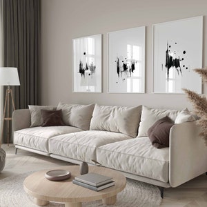 May include: A white sectional sofa with brown throw pillows sits in a living room with a wooden coffee table and a rug. Three black and white abstract art prints hang on the wall behind the sofa.