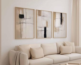 May include: Three framed abstract art pieces. Each features a beige background with black and tan geometric shapes and lines. The frames are a light wood color. The artwork hangs above a cream-colored sofa with matching pillows.