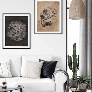 May include: Two black framed prints of tree rings on a white wall above a white couch with pillows and a throw blanket. A cactus and a potted plant are on the floor next to the couch.
