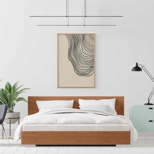 May include: A bedroom interior with a wooden bed frame, white bedding, and a black and white abstract print hanging on the wall. A green plant is in a pot on the floor, and a light blue nightstand with a black lamp is on the right side of the bed.