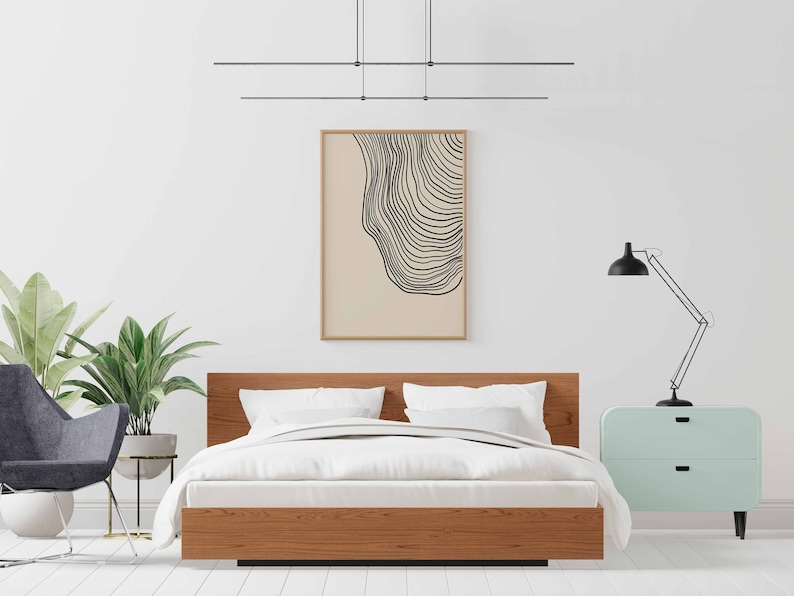 May include: A bedroom interior with a wooden bed frame, white bedding, and a black and white abstract print hanging on the wall. A green plant is in a pot on the floor, and a light blue nightstand with a black lamp is on the right side of the bed.
