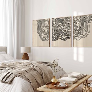May include: Three abstract line art prints in black and white with a beige background. The prints are framed in a light wood frame and are hung on a white wall.