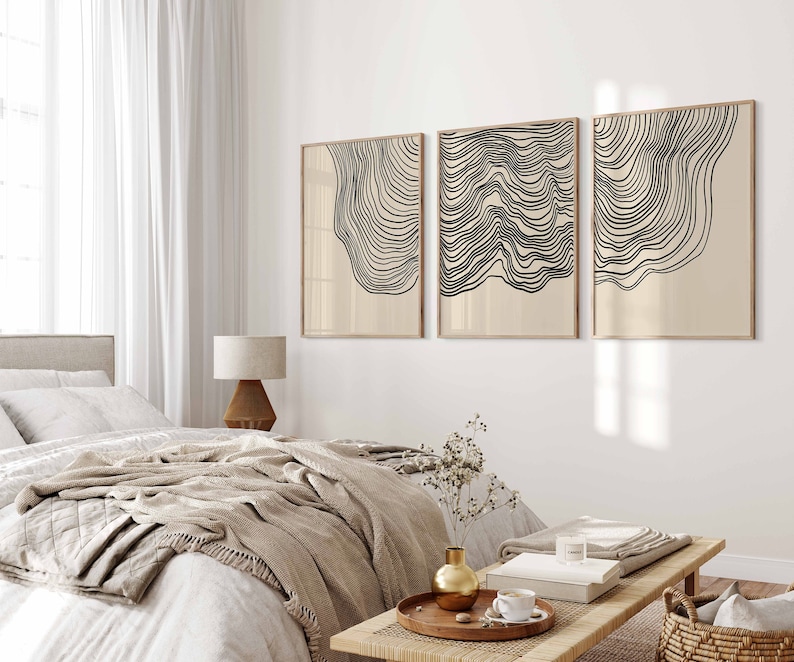 May include: Three abstract line art prints in black and white with a beige background. The prints are framed in a light wood frame and are hung on a white wall.