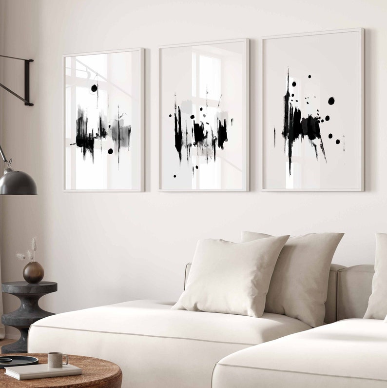 May include: Three black and white abstract art prints with a white background and black brushstrokes. The prints are framed in white and are hung on a white wall.