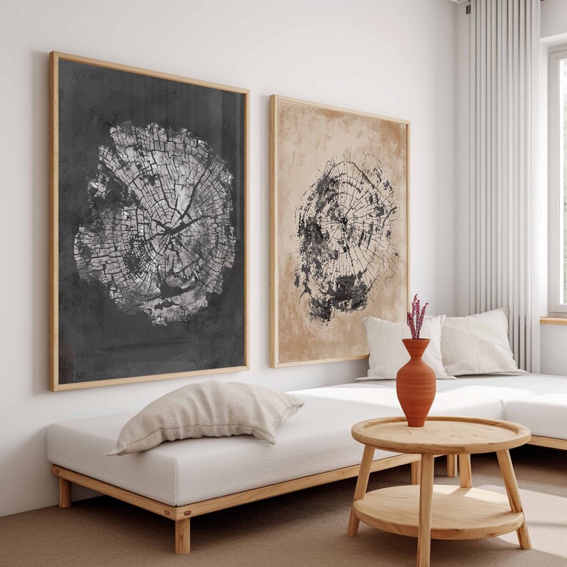 May include: Two framed black and white prints of tree rings on a light beige wall above a white futon with a light beige throw pillow. A small wooden table with a round top and two shelves sits in front of the futon. A terracotta vase with pink flowers sits on the table.